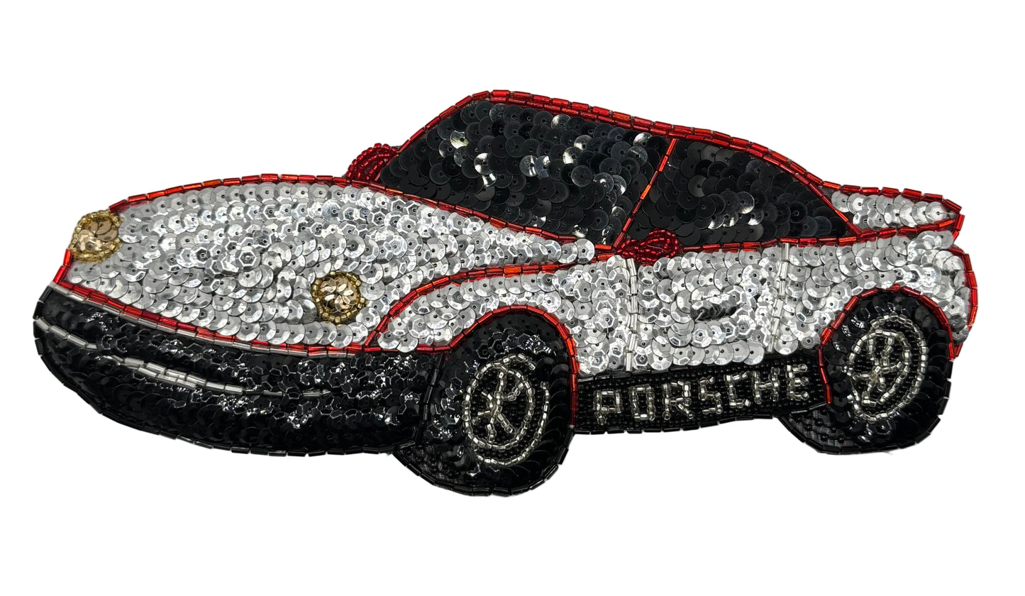 A vintage sequin patch in the shape of a Porsche car, predominantly silver and black in color with gold accents on the headlights.