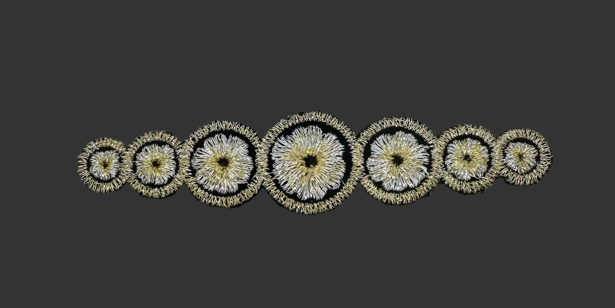 A decorative embroidered trim featuring a row of oval motifs with floral designs in black, white, and gold thread, laid flat on a light gray background.