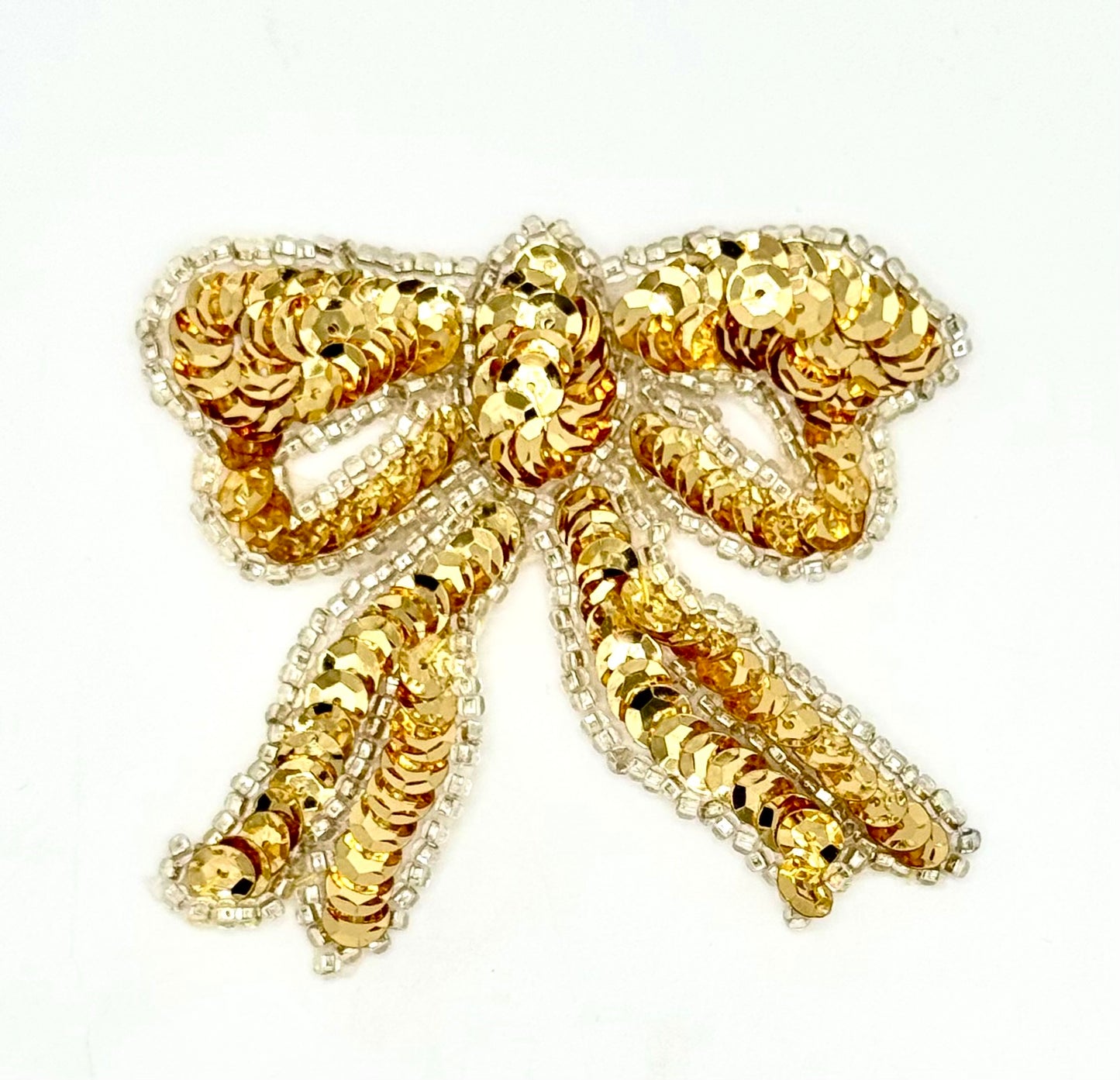 Gold bow-shaped brooch with sequins on a white background