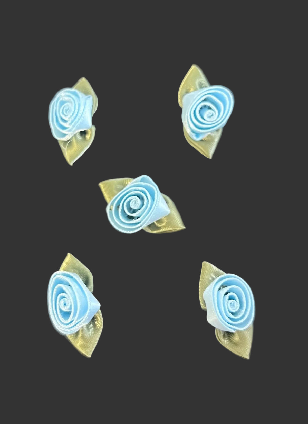 Five small light blue rolled rose-shaped satin flowers with pale green backing pieces, arranged on a dark textured surface.