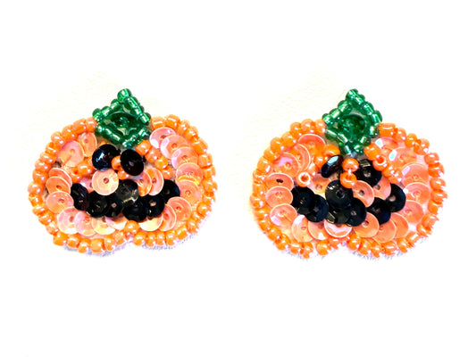 A pair of pumpkin-shaped beaded patches made from orange and pink sequins with green stems and black bead eyes and mouth, shown on a plain white background.