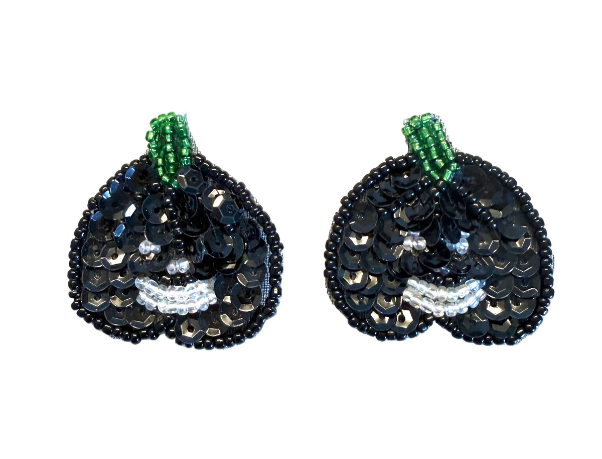 A pair of black sequined pumpkin-shaped embellishments with green beaded stems and white beaded mouth details, shown on a plain white background.