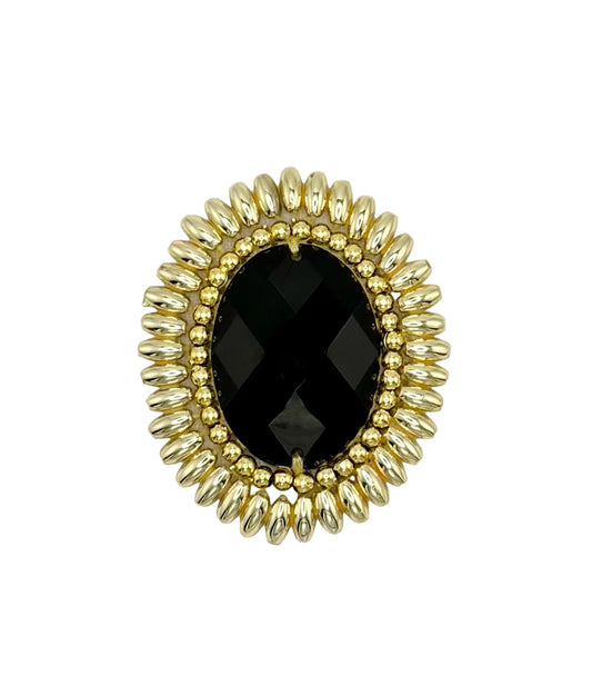 An oval brooch patch with a large faceted black center stone surrounded by a gold-tone beaded sunburst border, set against a plain white background.
