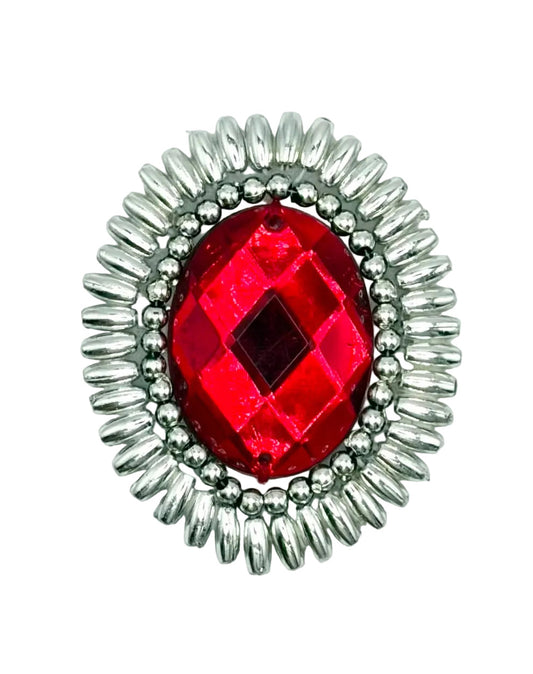 A silver-toned oval patch featuring a faceted red gemstone in the center, surrounded by a beaded border and a sunburst-style outer frame, shown on a plain white background.