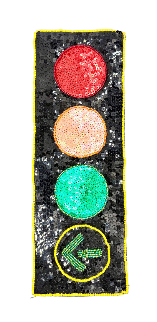 A rectangular black sequined patch featuring a vertical traffic light design with red, peach, green, and a green left-pointing arrow, outlined in yellow sequins on a white background.