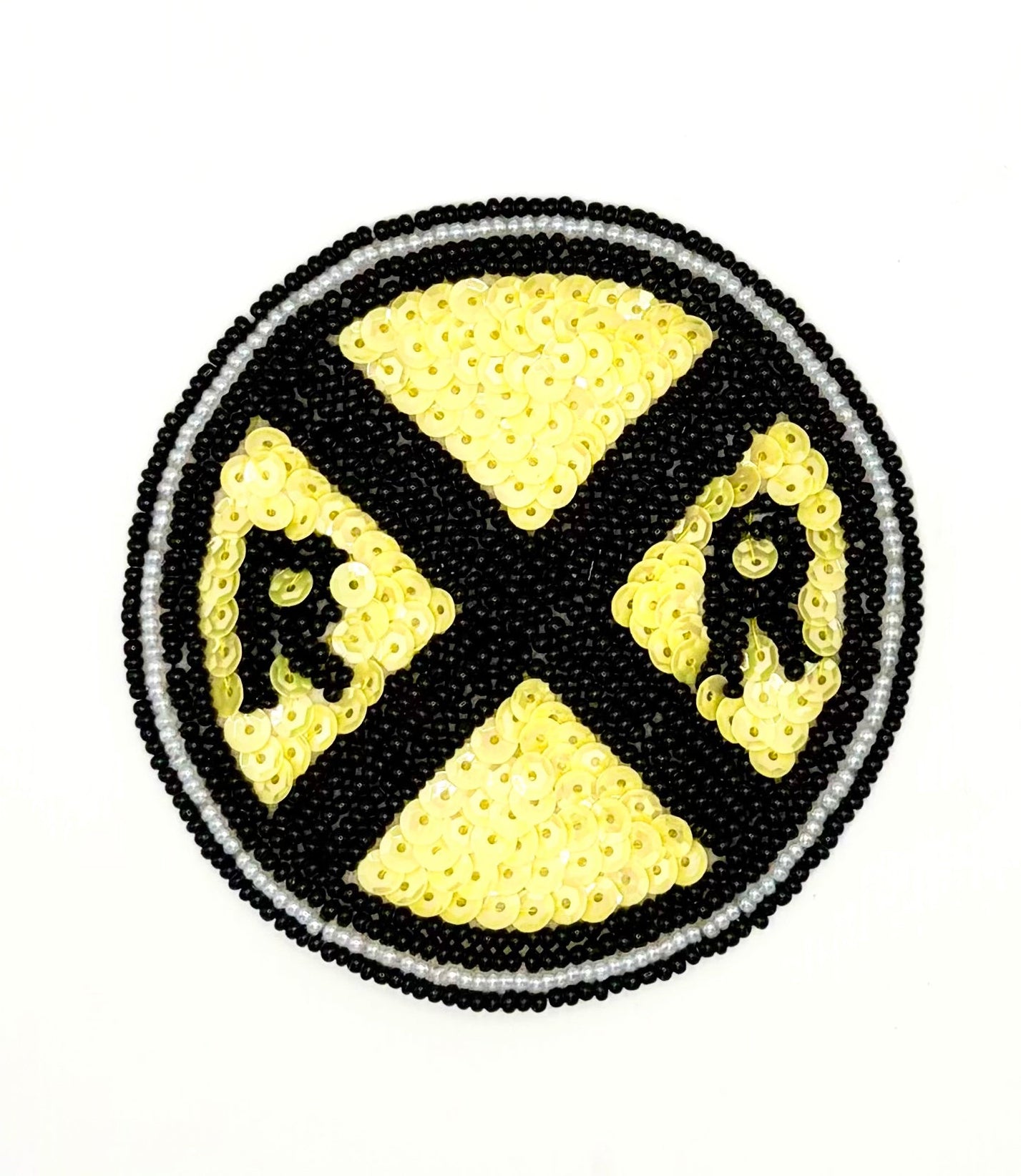 A circular sequin and bead patch featuring a railroad crossing road sign, constructed with black and yellow sequins and beads on a white background.