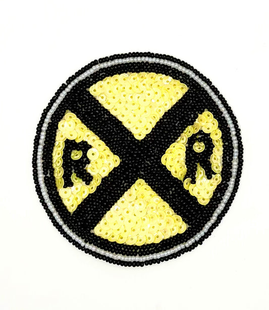 A circular sequin and bead patch featuring a railroad crossing road sign, constructed with black and yellow sequins and beads on a white background.