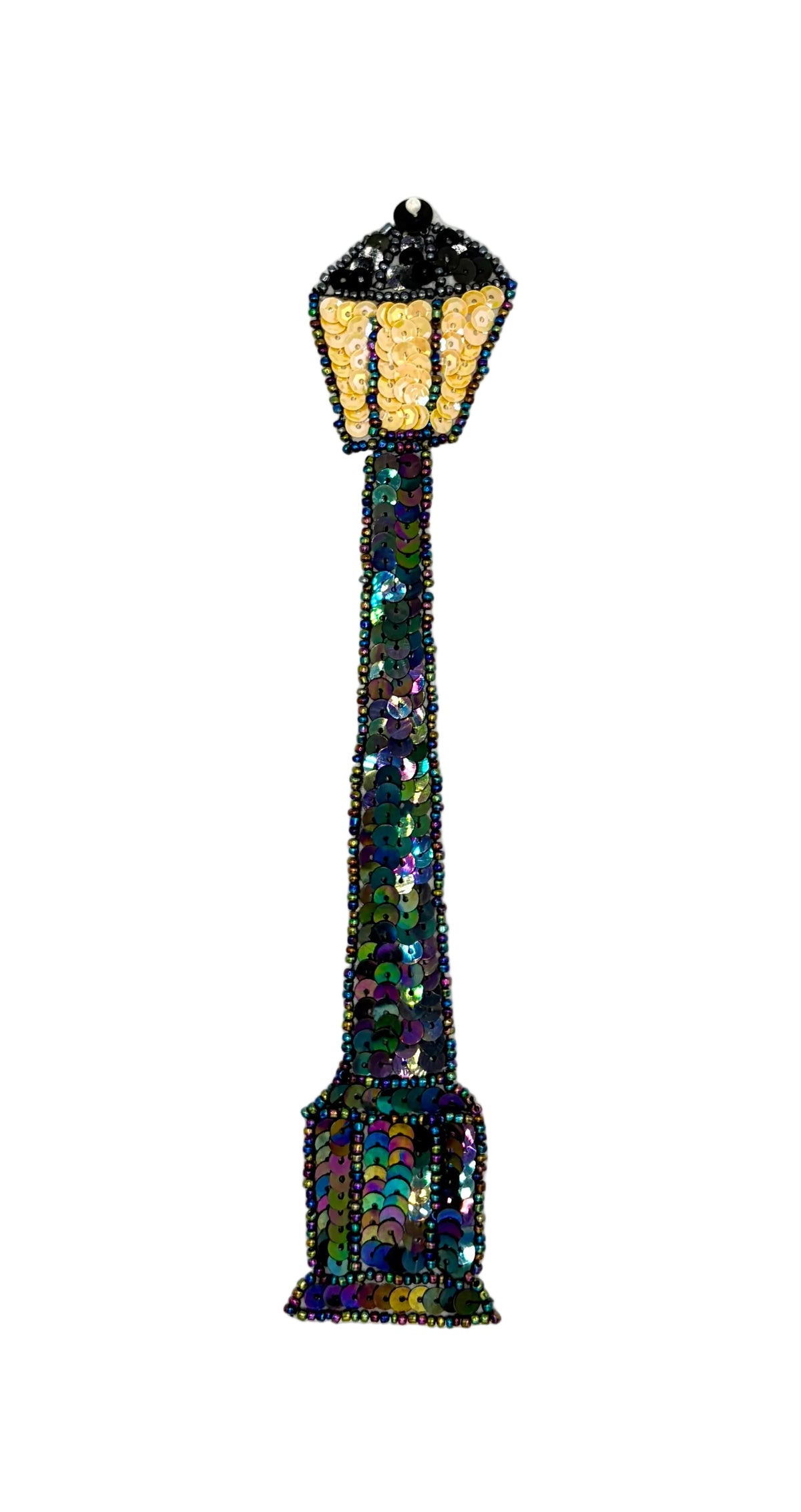 A decorative street lamp patch made of iridescent sequins and beads, featuring a glowing yellow lantern top and a dark, multicolored body, shown on a plain white background.