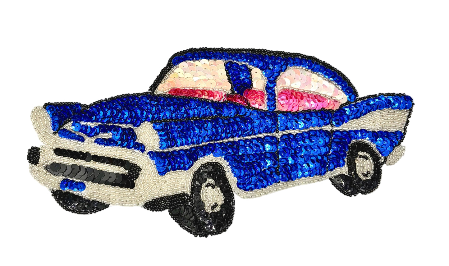 A vintage-style car patch or applique made from sequins, featuring a blue body, cream-colored bumpers and trim, black wheels, and pink-tinted windows, shown on a plain white background.