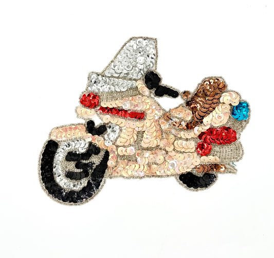 A decorative embroidered patch shaped like a motorcycle covered in sequins and beads. The patch features a mix of metallic silver, beige, black, red, brown, and blue sequins and beadwork, set against a plain white background.