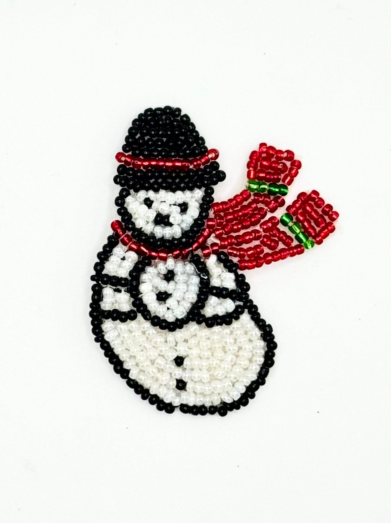 A beaded snowman ornament or patch featuring a black and white beaded body, a black hat with a red band, and a red scarf with green accents, shown on a plain white background.