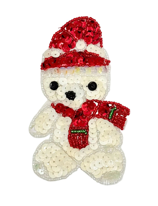 A sequined teddy bear applique featuring a white body with red sequined hat and scarf, black sequin eyes and nose, and small green accent details on the scarf, shown on a plain white background.