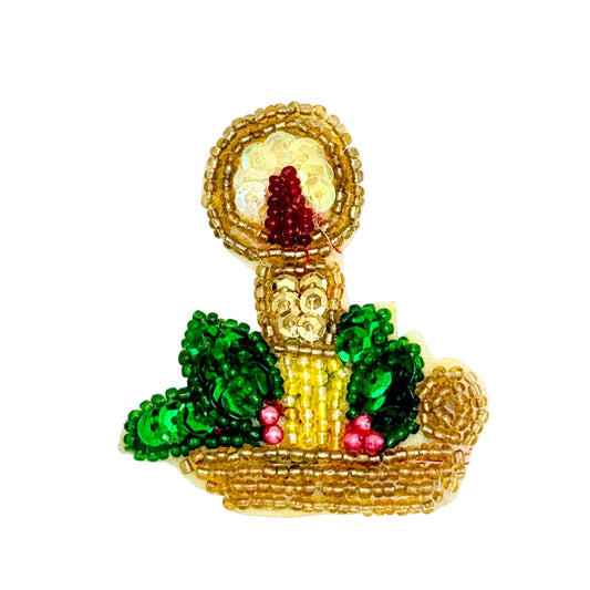 A handcrafted beaded Christmas candle appliqué  with green sequined leaves, pink berry accents, and a gold-toned candle inside, set against a plain white background.