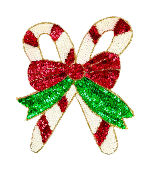 A sequined Christmas bow and candy cane design on a plain white background. The bow and candy cane are decorated with red, green, and white sequins, outlined with gold thread.