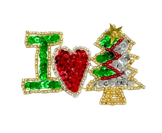 A handmade holiday-themed embellishment spelling 'I' followed by a red heart and a Christmas tree, crafted with green, red, silver, and gold sequins and beads on a white background.