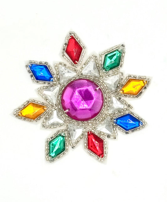 A colorful starburst patch featuring a central pink gemstone surrounded by red, blue, green, and yellow gemstones in a silver-tone setting, shown on a plain white background.