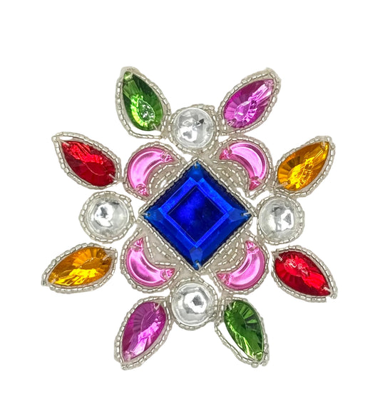 A decorative floral appliqué featuring a central royal blue diamond-shaped crystal surrounded by pink crescent-shaped stones, red and yellow teardrop-shaped stones, green teardrop-shaped stones, and silver rhinestone accents on a plain white background.