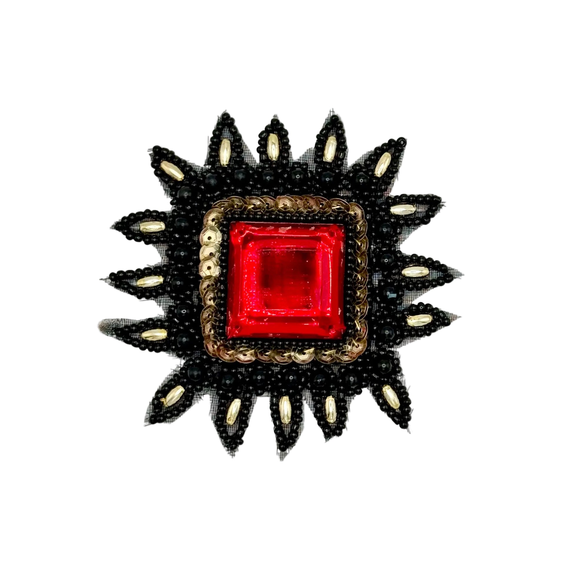 A decorative beaded patch featuring a central square red gemstone surrounded by a gold-toned border, with black beaded rays extending outward and small white accents along the points.