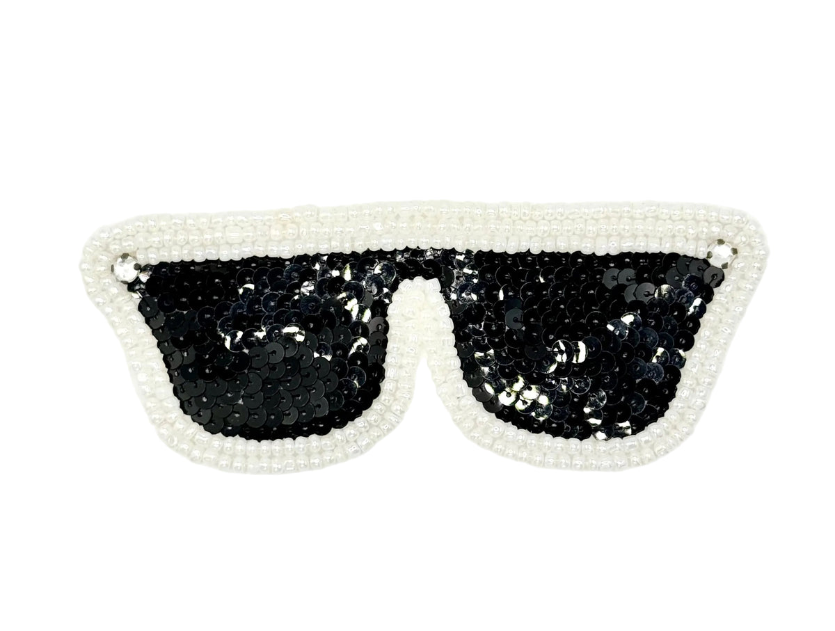 A novelty costume patch shaped like sunglasses, featuring black sequined lenses and a white beaded frame on a white background.