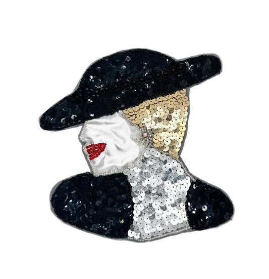 A sequined fashion accessory patch shaped like a woman's head in profile, featuring a black hat, silver face, red lips, and black, gold, and silver sequin details on a plain light background.