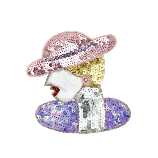A stylized appliqué of a woman in profile, decorated with pink sequins in a hat, gold sequins in the hair, a white face area, red lips, and a lavender-and-silver sequined dress on a plain light background.