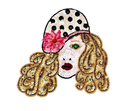 A decorative embroidered patch of a stylized woman's face with gold sequined hair, a pink flower and polka-dot hat, and a white face, shown on a plain white background.