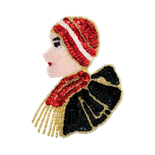 A decorative sequin patch of a woman in profile wearing a red and white sequined hat, a red sequined scarf, and a black sequined dress with gold beaded outlines, shown on a plain white background.
