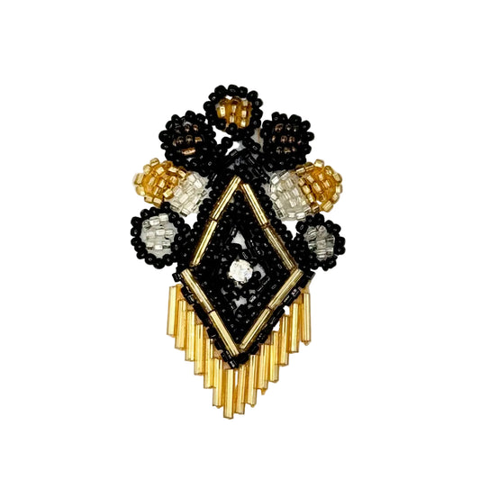 A handcrafted beaded crest design featuring a central diamond motif in black and gold beads, surrounded by floral clusters with black, white, and gold seed beads, and a fringe of gold beads at the bottom, displayed on a clean white background.