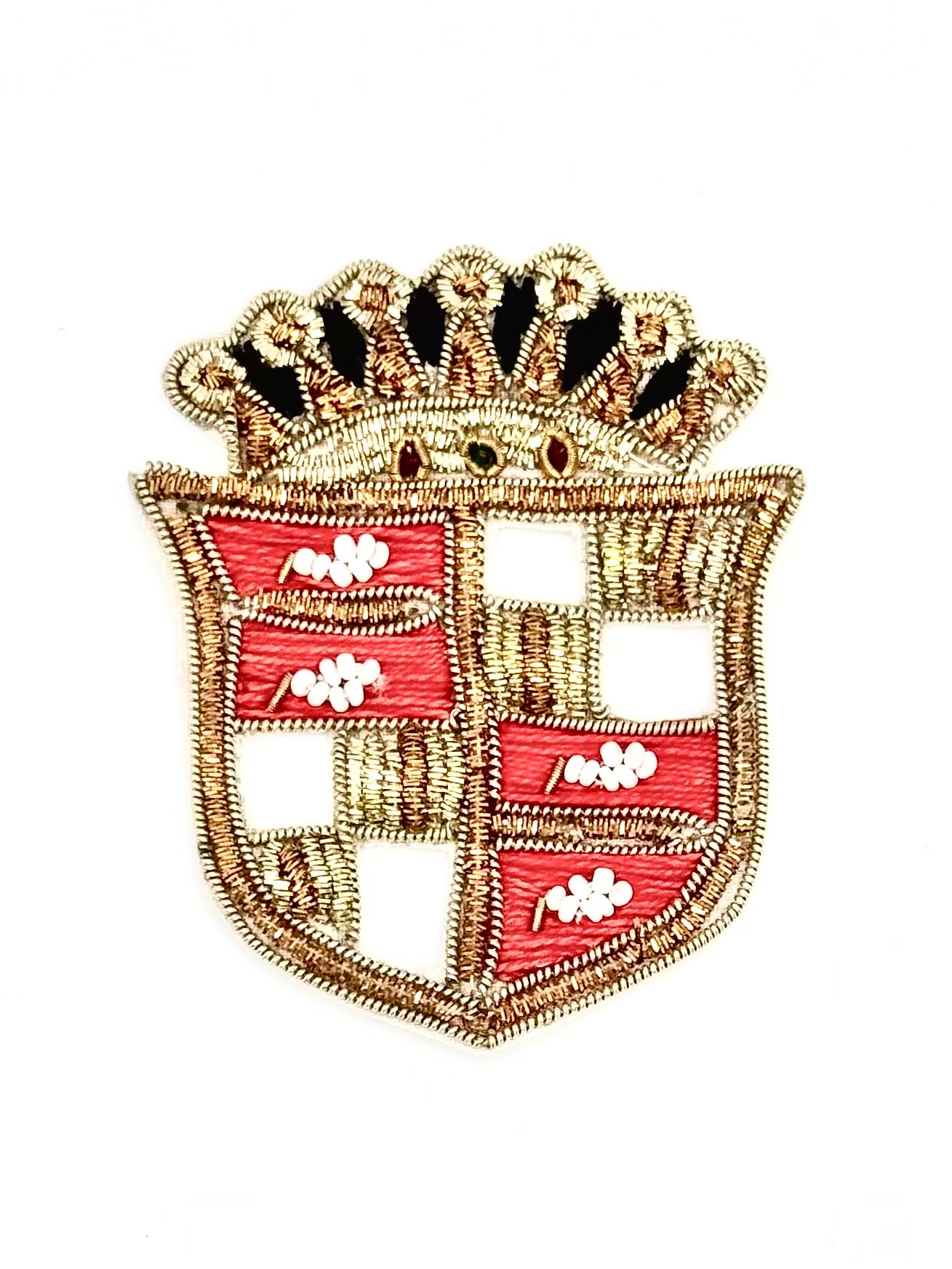 An embroidered shield-shaped patch with a gold-tone crown and border, featuring alternating red and open sections with small white floral motifs, shown on a plain white background.