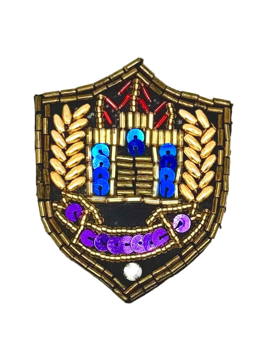 A shield-shaped beaded patch with a bronze metallic beaded border, featuring blue and purple sequins, red accents, and gold leaf-like beads on a white background.