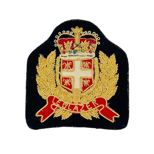 An embroidered military-style crest patch on a black fabric background, featuring a gold crown, laurel branches, a white cross on a red shield, and a red scroll with gold lettering, photographed against a plain white background.