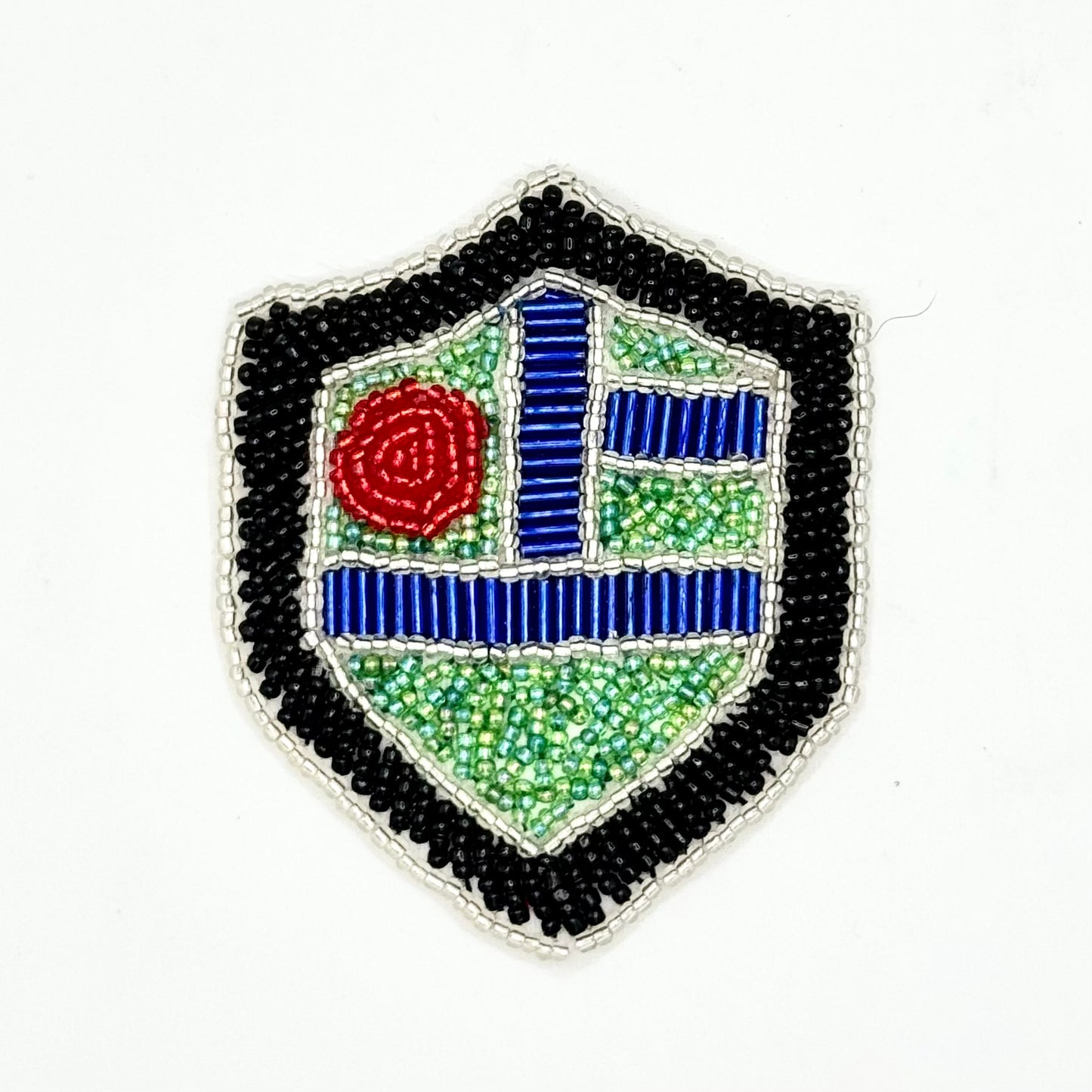 A shield-shaped beaded patch featuring a black outer border, a silver inner border, turquoise geometric sections, a red circular bead motif, and Royal Blue lines, photographed on a plain white background.