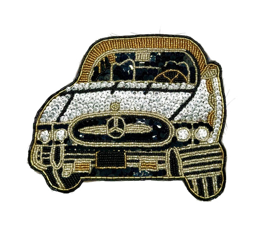 A vintage sequin and bead patch of a vintage Mercedes-Benz car, embellished with rhinestones on the hood and grille, featuring gold and black thread on a white background.