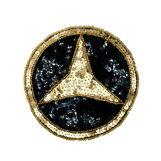 A vintage circular Mercedes-Benz star patch embellished with gold sequins and black sequins, set against a light gray textured background.