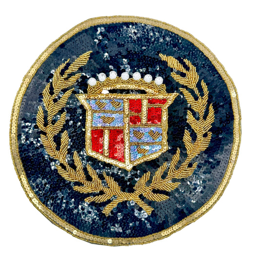A circular vintage sequin and bead patch featuring a gold laurel wreath and a shield with red, blue, and white details, set against a black sequined background on a white backdrop.