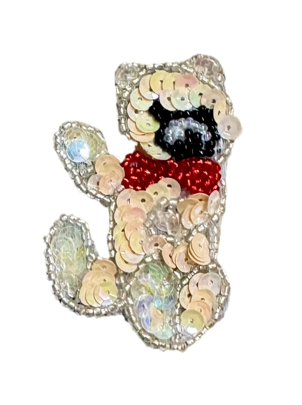 A teddy bear-shaped embellished brooch or pin made of iridescent sequins, featuring a black face, red beaded scarf, and silver-toned sequined border on a plain white background.