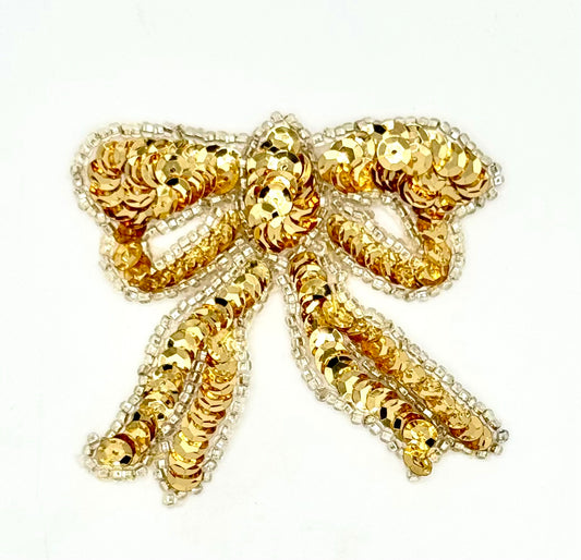 Gold bow-shaped brooch with sequins on a white background