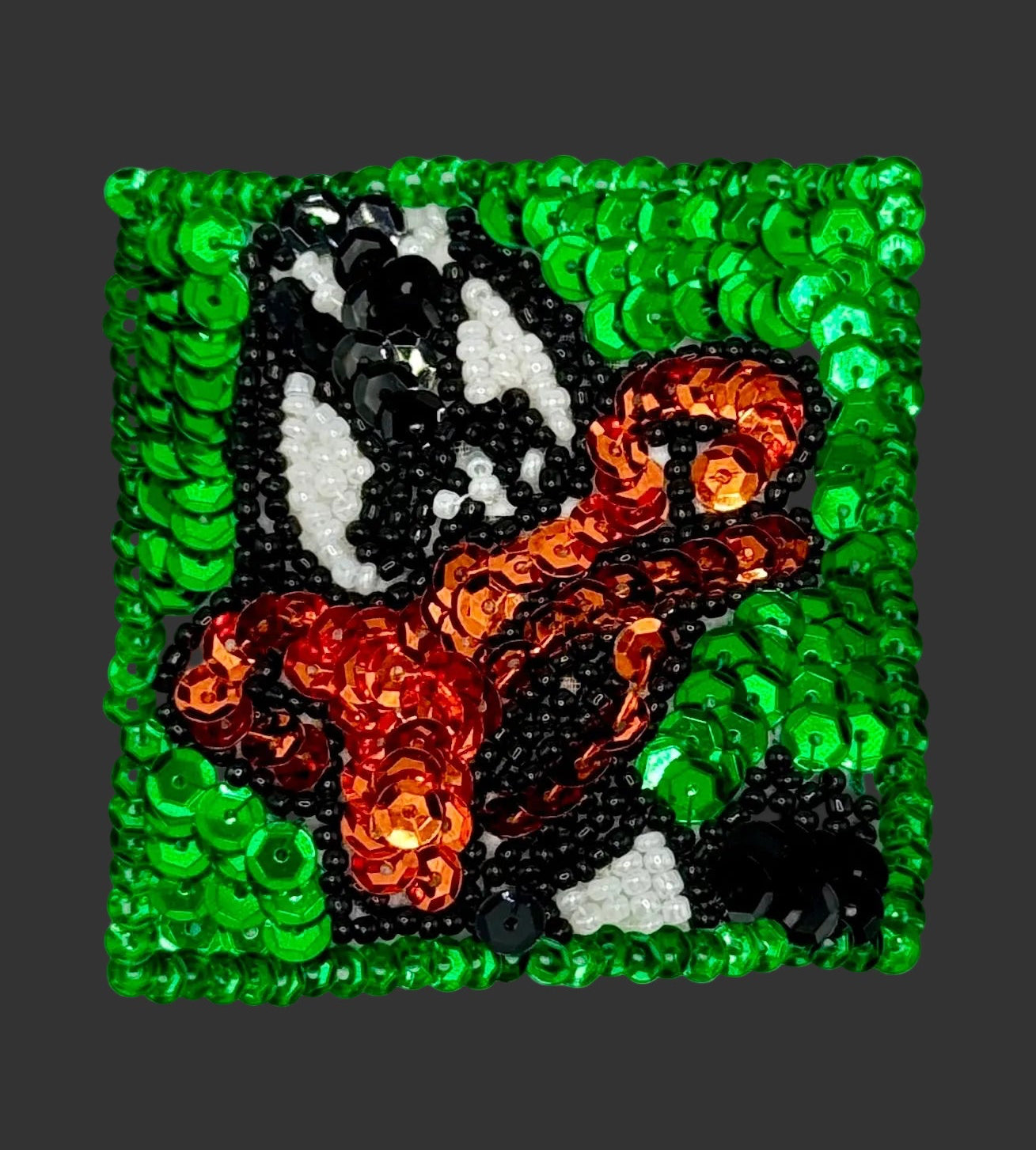 Square patch with duck design surrounded by green sequins on a black background