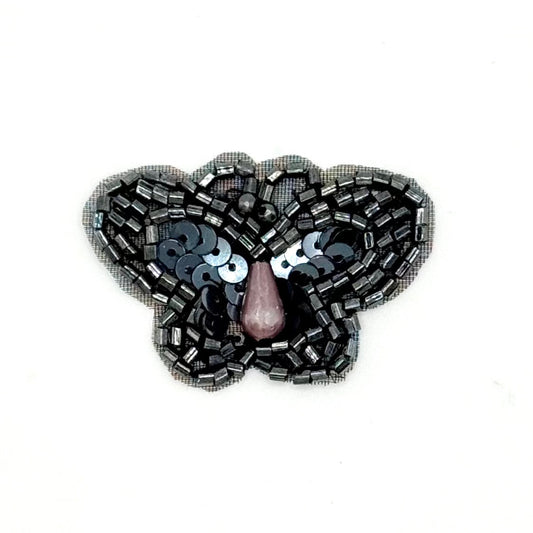 Sequin gunmetal colored butterfly-shaped brooch with sequins on a white background