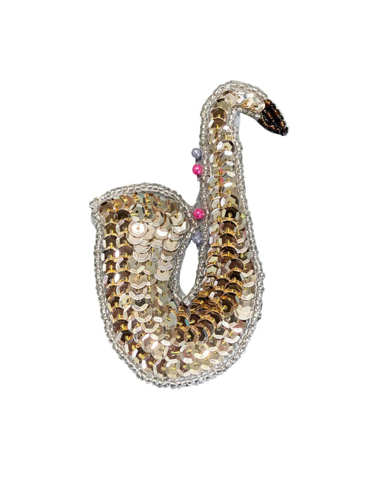 A sequin saxophone embellished with gold and silver sequins, featuring a small pink gem and a black beak, set against a plain white background.