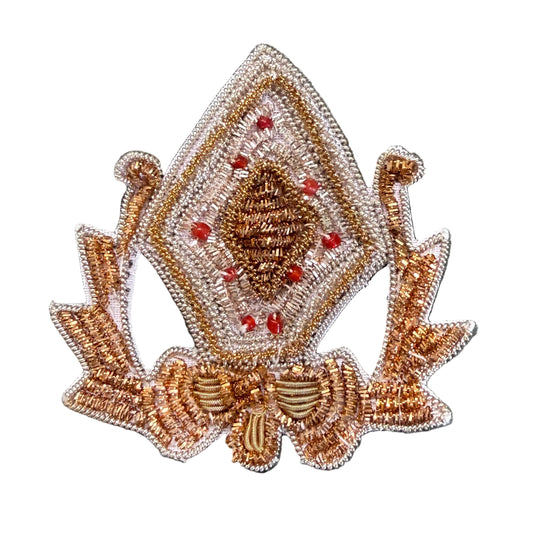 A decorative embroidered patch featuring a diamond-shaped design with a central pinecone motif, surrounded by red berry-like accents and a bow at the bottom.