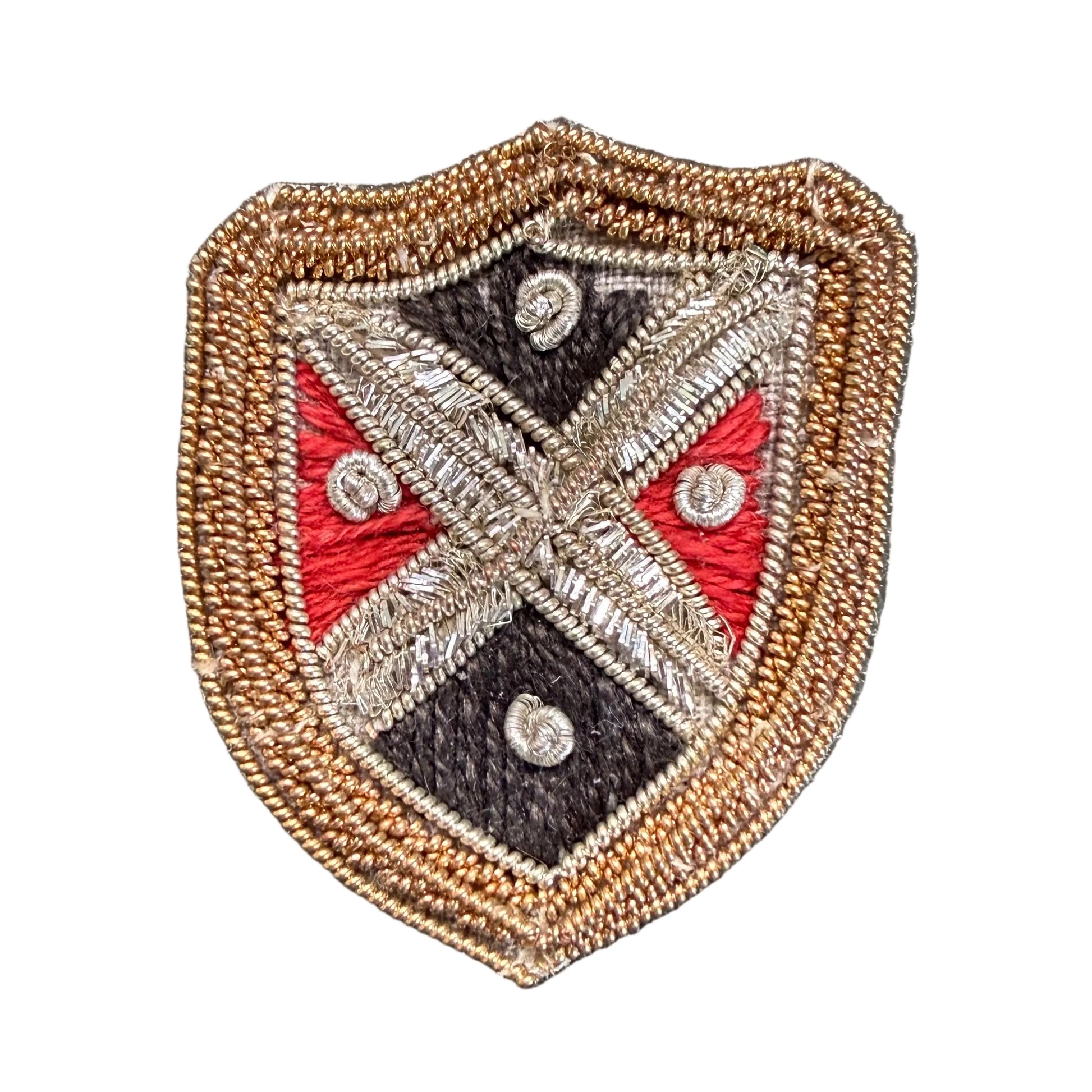 An embroidered shield-shaped patch with a tan border, featuring a black, red, and silver cross design.