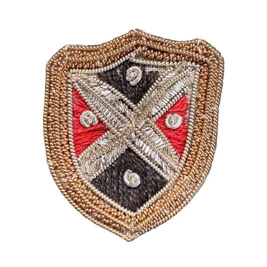 An embroidered shield-shaped patch with a tan border, featuring a black, red, and silver cross design.